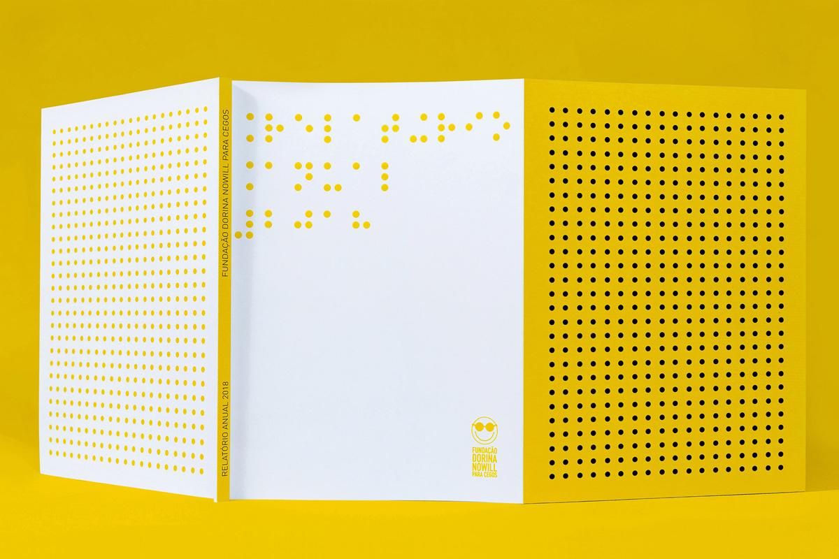 Relatório anual da Fundação Dorina Nowill aberto sobre fundo amarelo, com pontos de Braille impressos e em relevo